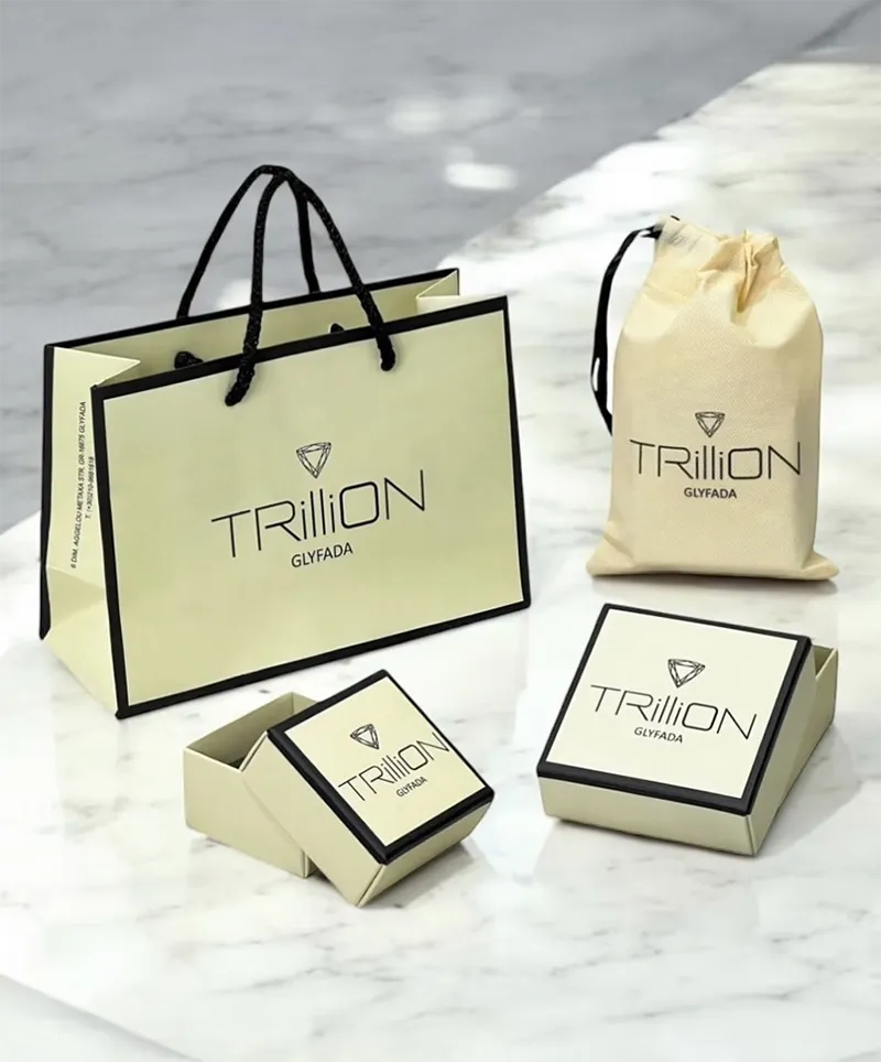 A matching set of "TRILLION GLYFADA" luxury packaging, including a paper bag, a drawstring pouch, and two small gift boxes, is neatly arranged on a white marble surface.